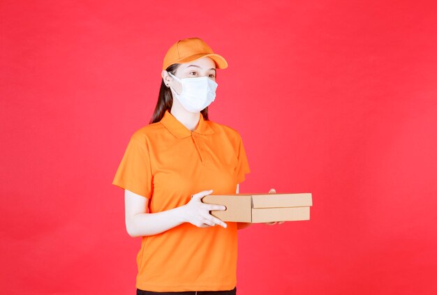 Female courier in orange color dresscode and mask holding a cardboard box