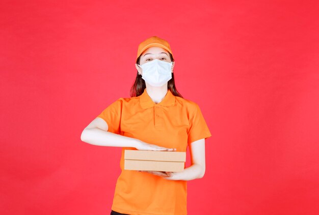 Female courier in orange color dresscode and mask holding a cardboard box