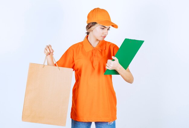 마분지 쇼핑백을 들고 녹색 고객 목록을 확인하는 주황색 제복을 입은 여성 택배