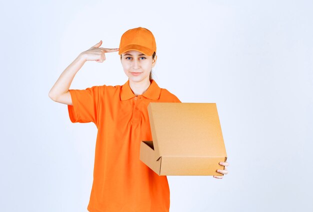 Female courier in orange uniform holding an open cardboard box and looks confused and thoughtful