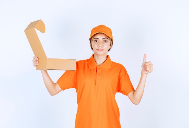 Female courier in orange uniform holding an open cardboard box and showing enjoyment sign