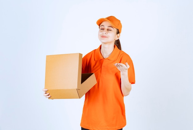 Corriere femminile in uniforme arancione con in mano una scatola di cartone aperta e annusare il prodotto all'interno. Foto Gratuite