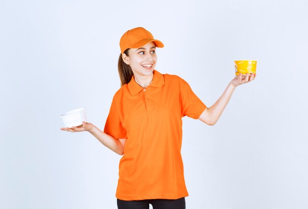 Female courier in orange uniform holding plastic and yellow noodles cup in both hands