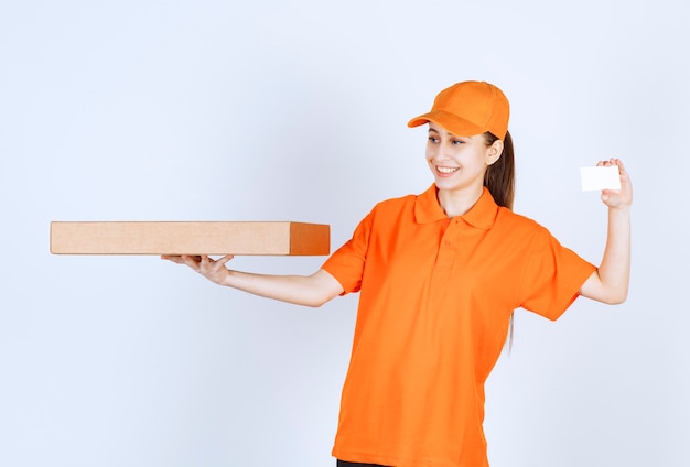Женский курьер в оранжевой форме держит коробку для пиццы на вынос и представляет свою визитную карточку.