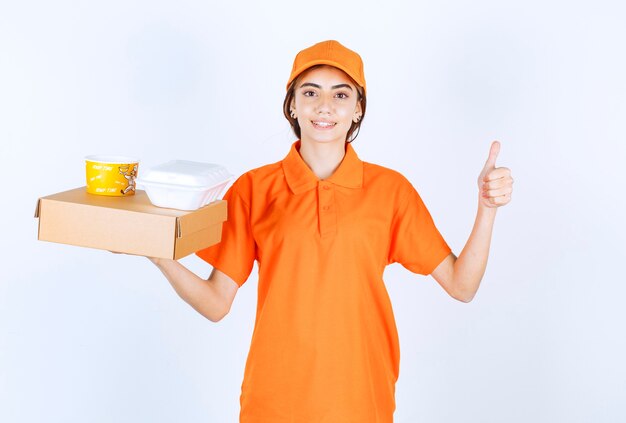 Female courier in orange uniform holding yellow and white takeaway boxes