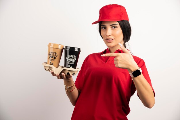 Женский курьер, указывая на чашки кофе. Фото высокого качества