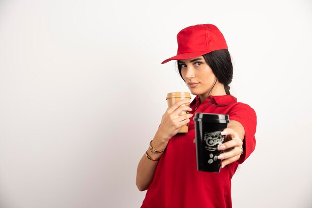 Female courier in red uniform giving away a cup of coffee. High quality photo