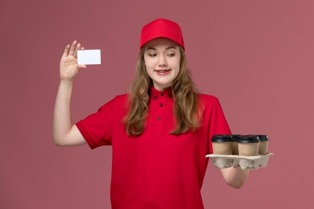 갈색 배달 커피 컵과 카드를 들고 빨간 제복을 입은 여성 택배 작업자에게 분홍색, 균일 한 서비스 제공