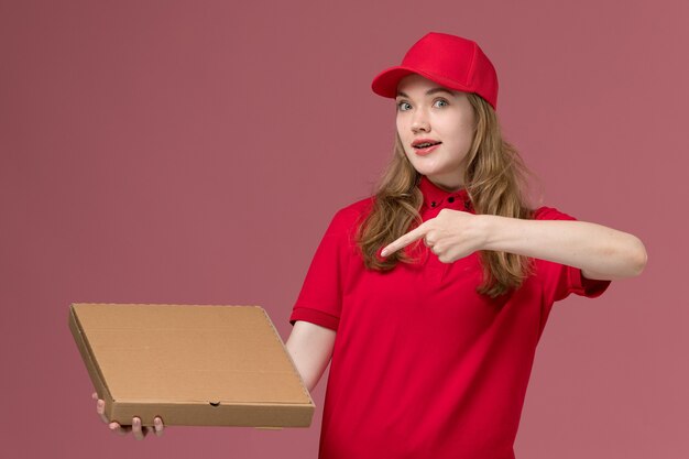 female courier in red uniform holding brown food box on pink, uniform job worker service delivery