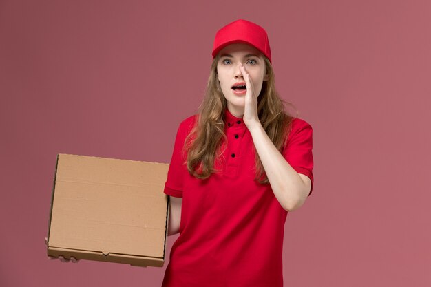 female courier in red uniform holding brown food delivery box and whispering on the pink, uniform service delivery job worker