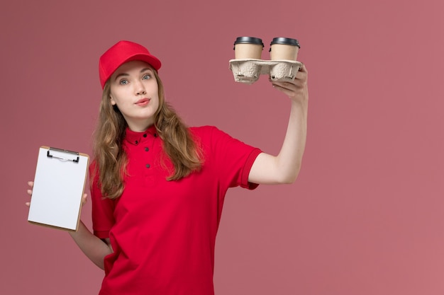 female courier in red uniform holding coffee cups and notepad on pink, uniform service delivery job worker