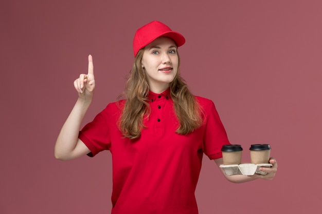 female courier in red uniform holding coffee cups on pink, uniform job service delivering worker