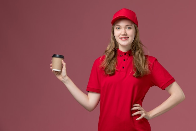 ピンクのポーズをとって笑顔で配達コーヒーカップを保持している赤い制服を着た女性の宅配便、仕事の制服労働者サービスの配達