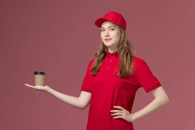 female courier in red uniform holding delivery coffee posing on light pink, job uniform worker service delivery