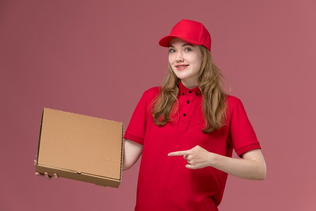 женщина-курьер в красной форме держит коробку для доставки еды на светло-розовом, рабочая форма службы доставки