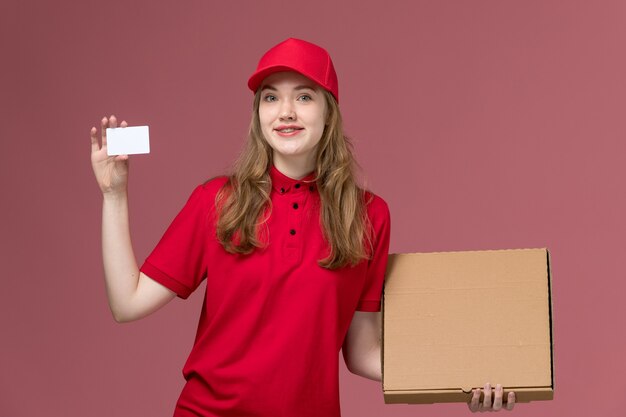 female courier in red uniform holding delivery white card food box on light pink, uniform job service worker delivery girl