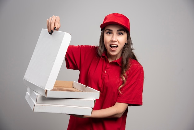 Female courier in red uniform holding empy pizza box on gray wall
