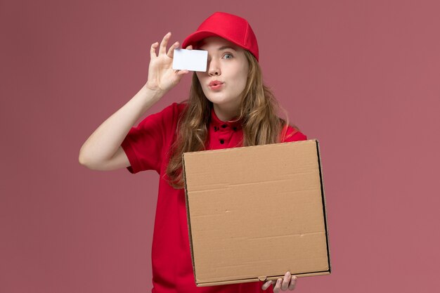 female courier in red uniform holding food box and card on pink, uniform service delivery job worker