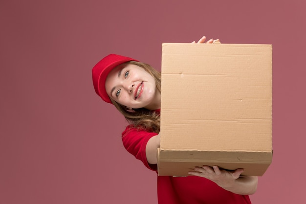 Foto gratuita corriere femminile in uniforme rossa che tiene la scatola di cibo sorridente sul lavoro rosa, uniforme dell'operaio di consegna del servizio