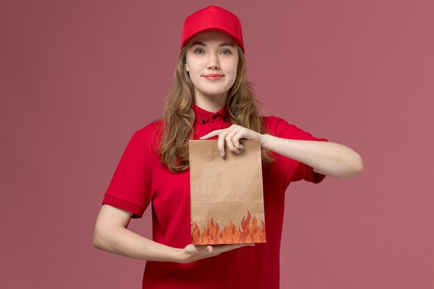 female courier in red uniform holding food package on ight-pink, job uniform service worker delivery