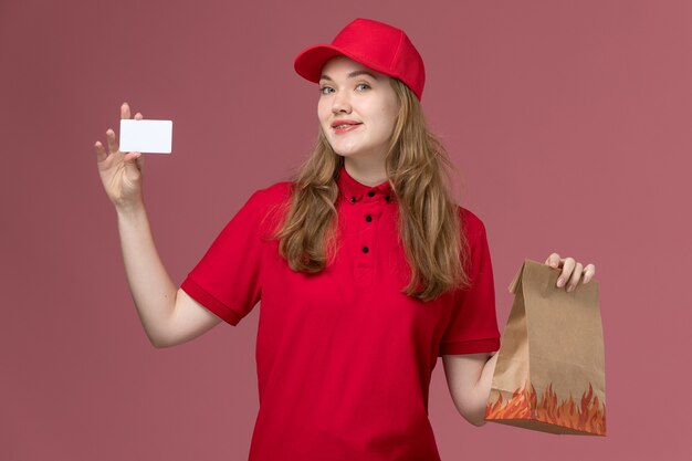 female courier in red uniform holding food package white card on pink, uniform service delivery job worker