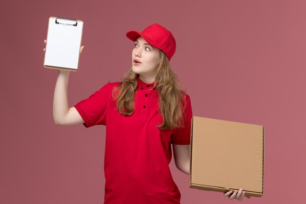 female courier in red uniform holding notepad and food box on light pink, job uniform service worker delivery