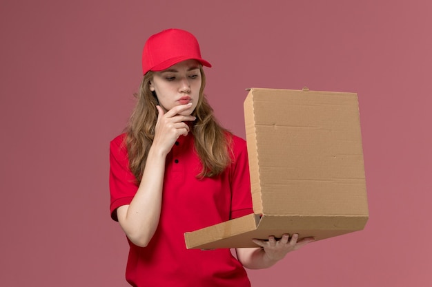 赤い制服を着た女性の宅配便、淡いピンクの配達ボックスを保持して開く、仕事の制服サービスワーカーの配達