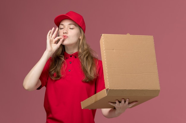 Foto gratuita corriere femminile in uniforme rossa che tiene e che apre la scatola di cibo sul rosa, lavoratore uniforme che consegna il servizio