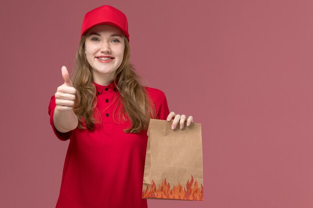 female courier in red uniform holding paper food package on the light-pink, job uniform worker service delivery