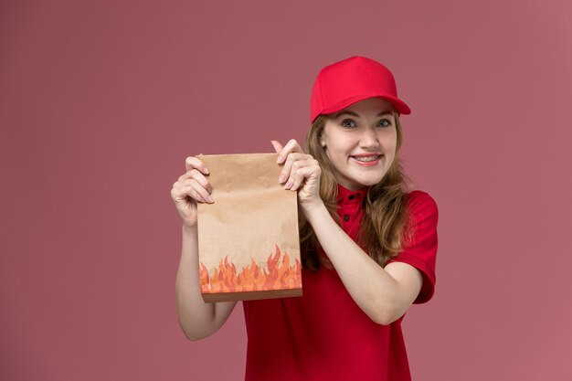 ピンクの笑顔で紙の食品パッケージを保持している赤い制服を着た女性の宅配便、仕事の制服労働者サービスの提供