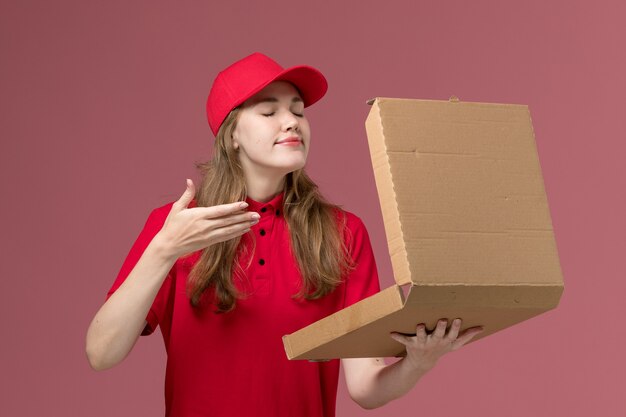 female courier in red uniform holding smelling food box on pink, uniform service delivery job