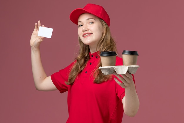 female courier in red uniform holding white card coffee on pink, uniform service delivering worker
