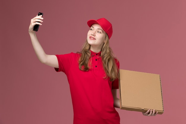 female courier in red uniform taking selfie with food box on pink, uniform job service worker delivering worker