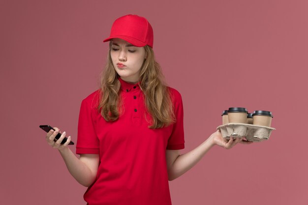 ピンクの制服サービス提供の仕事の労働者にコーヒーカップを保持している彼女のスマートフォンを使用して赤い制服を着た女性の宅配便
