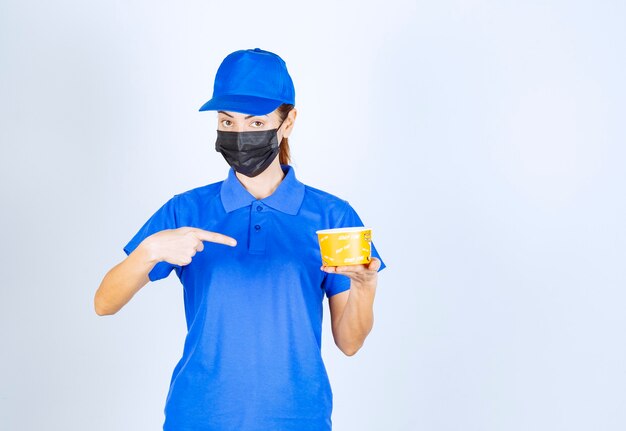 파란색 유니폼을 입은 레스토랑의 여성 택배와 테이크아웃 음식을 들고 있는 얼굴 마스크.