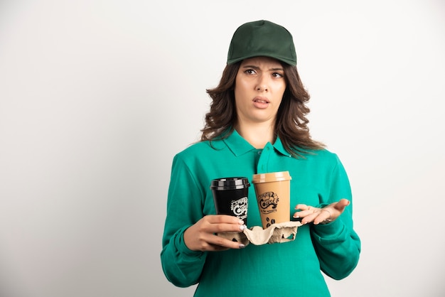 Женский курьер в униформе, держащий кофе на вынос с безумным выражением лица.