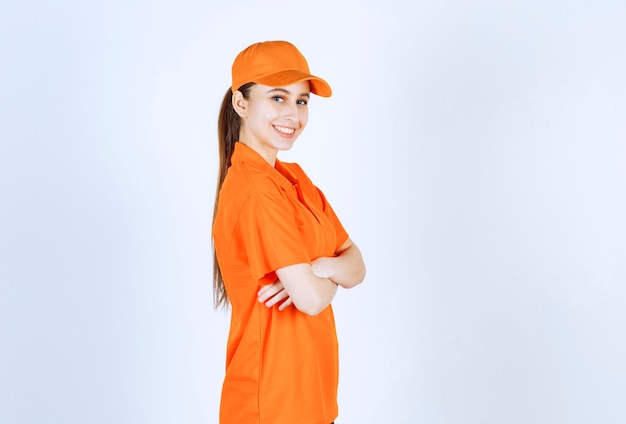 Female courier wearing orange uniform and cap crossing arms and giving professional look