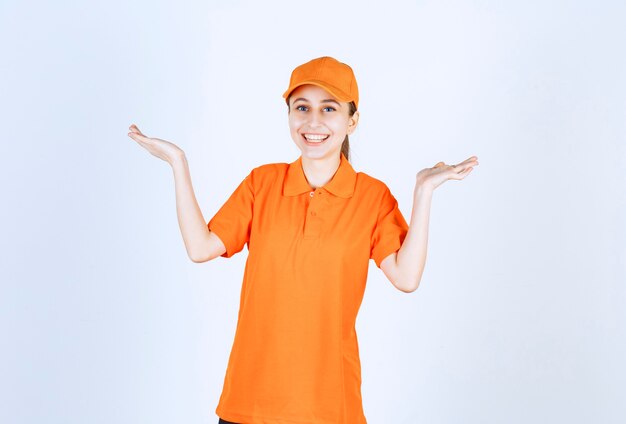 Женский курьер в оранжевой форме и кепке, указывающей в обе стороны.