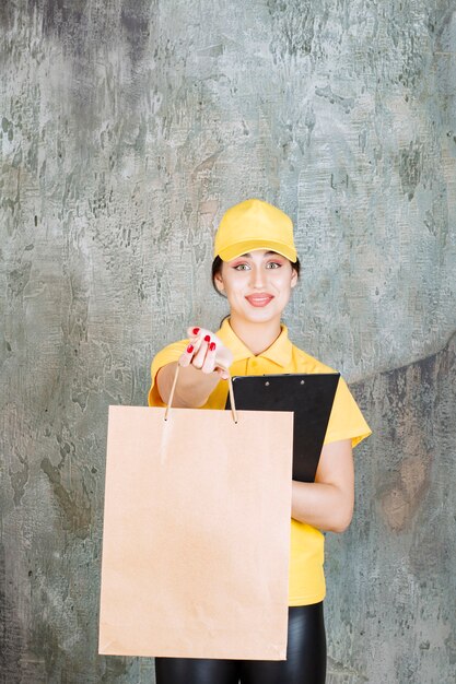 Female courier wearing yellow uniform delivering a cardboard shopping bag and holding a black folder