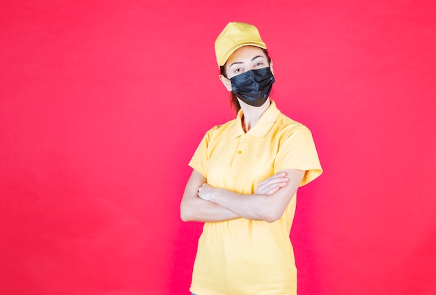 黄色の制服と黒のマスクの交差する腕と自信を持って見える女性の宅配便