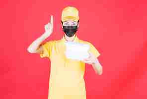 Free photo female courier in yellow uniform and black mask holding multiple takeaway packages and having a good idea