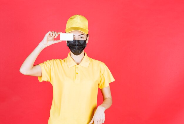 Female courier in yellow uniform and black mask presenting her business card