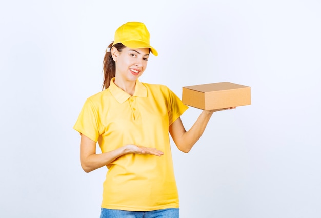 Female courier in yellow uniform delivering a cardboard parcel and feeling positive. 