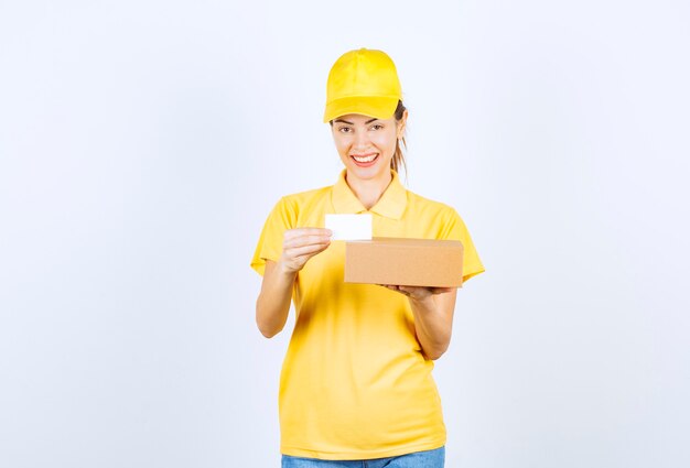 Corriere femminile in uniforme gialla che consegna un pacco e offre il suo biglietto da visita.