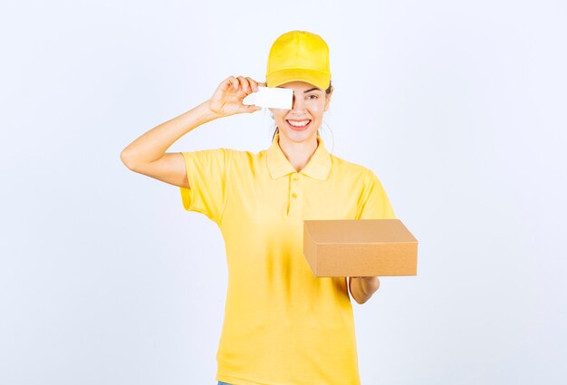 Female courier in yellow uniform delivering a parcel and offering her business card. 
