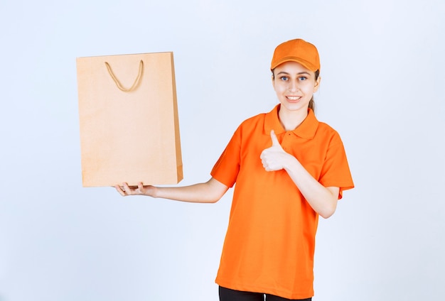 Female courier in yellow uniform delivering a shopping bag and showing positive hand sign.