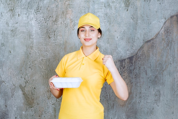 Female courier in yellow uniform delivering a white takeaway box and showing her arm muscles.