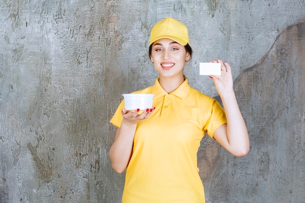 Female courier in yellow uniform holding a takeaway cup and presenting her business card.