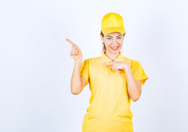 Female courier in yellow uniform showing something on the left. 