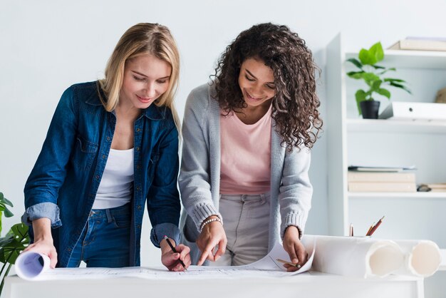 Female coworkers leaning over paper floor plan drawing 